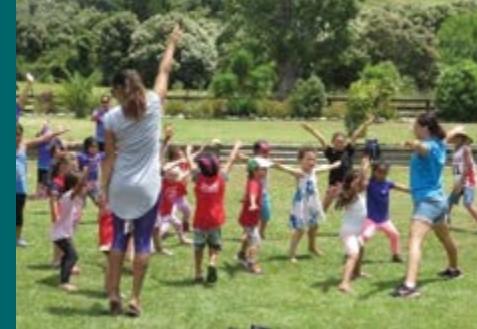 Two teachers and a group of 10 children do exercises outdoors on the grass.